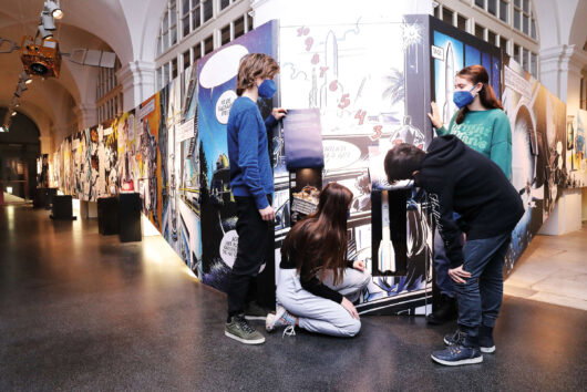 Kinder in der Ausstellung "Mission Possible" im Grazer Joanneum vor riesigen Comic-Illustrationen von Chris Scheuer 