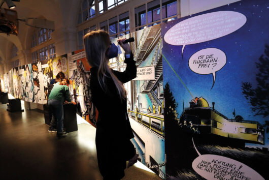Ein junges Mädchen in der Ausstellung "Mission Possible" im Grazer Joanneum vor riesigen Comic-Illustrationen von Chris Scheuer 